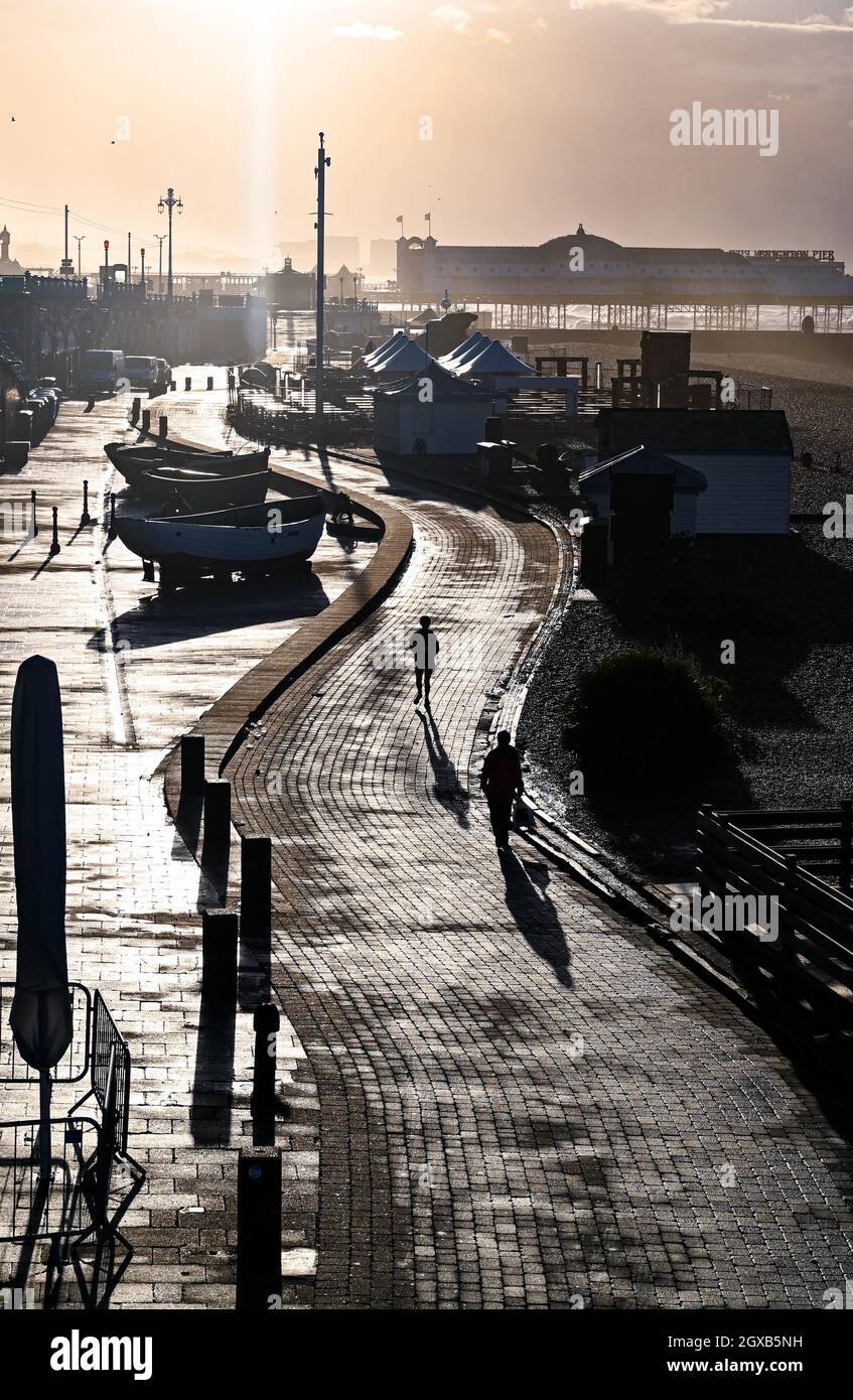 Brighton UK 2. Oktober 2021 - Spaziergänger am frühen Morgen an der Küste von Brighton, wenn die Sonne nach einer Nacht mit starkem Regen und starken Winden im Südosten Großbritanniens aufgeht : Credit Simon Dack / Alamy Live News Stockfoto