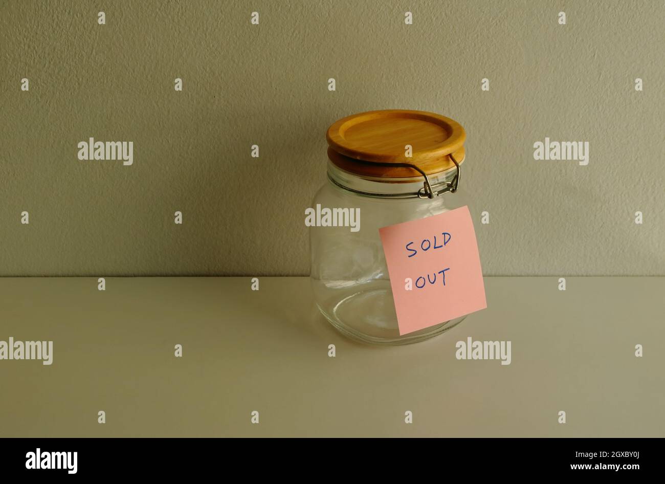 Selektiver Fokus auf Klebenote mit ausverkaufter Nachricht, die an einem Glas angebracht ist, das auf einem Holztisch gegen die Zementwand platziert ist Stockfoto