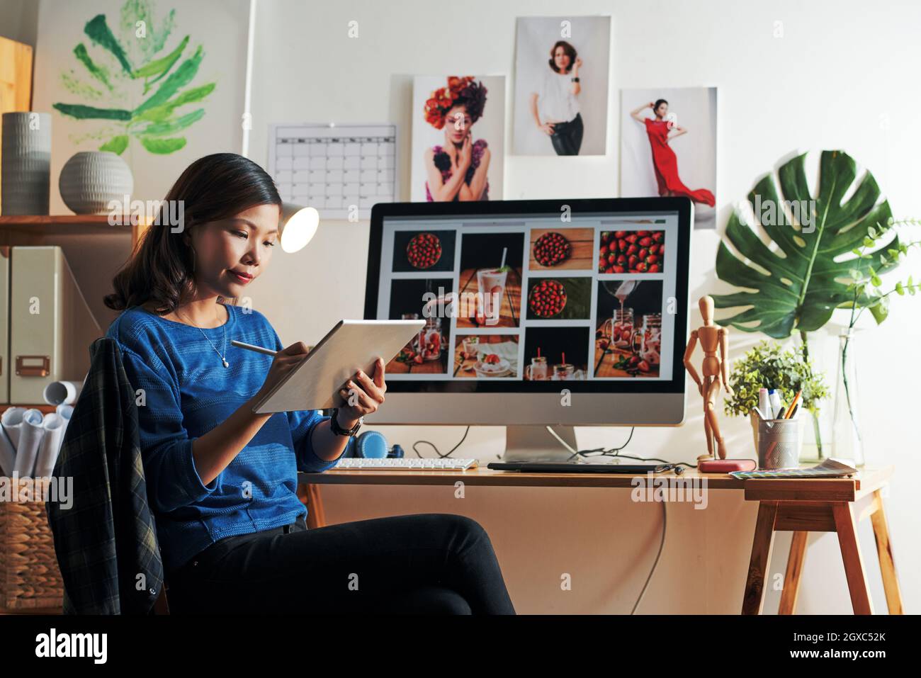 Attraktive junge asiatische Frau sitzt am Computer mit Erdbeerbildern auf dem Bildschirm und Zeichnung Skizze auf Tablet Stockfoto