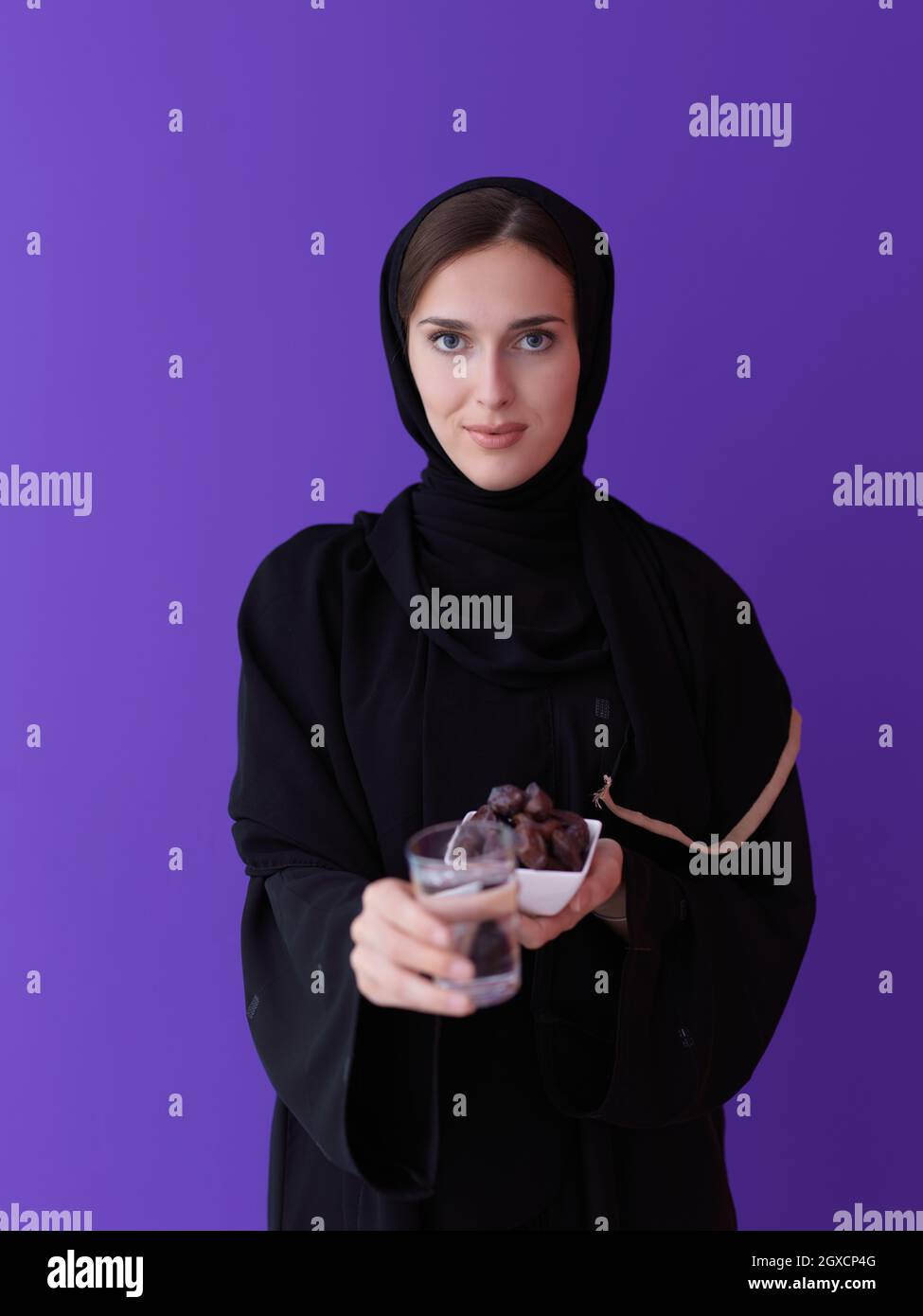 Moderne muslimische Frau in Abaya hält eine Dattefrucht und ein Glas Wasser von ihr. Konzept Feier des iftar im ramadan und Ende des Festes Stockfoto