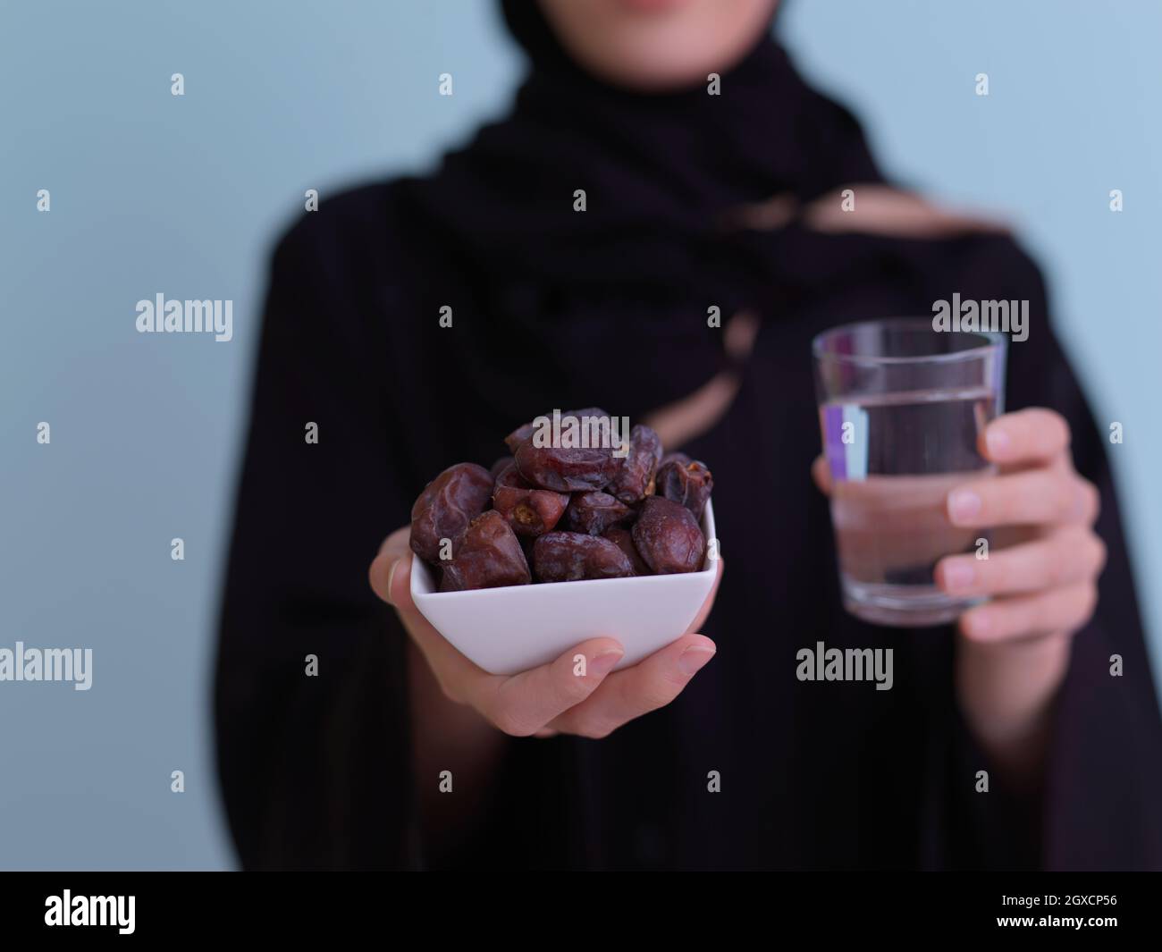 Moderne muslimische Frau in Abaya hält eine Dattefrucht und ein Glas
