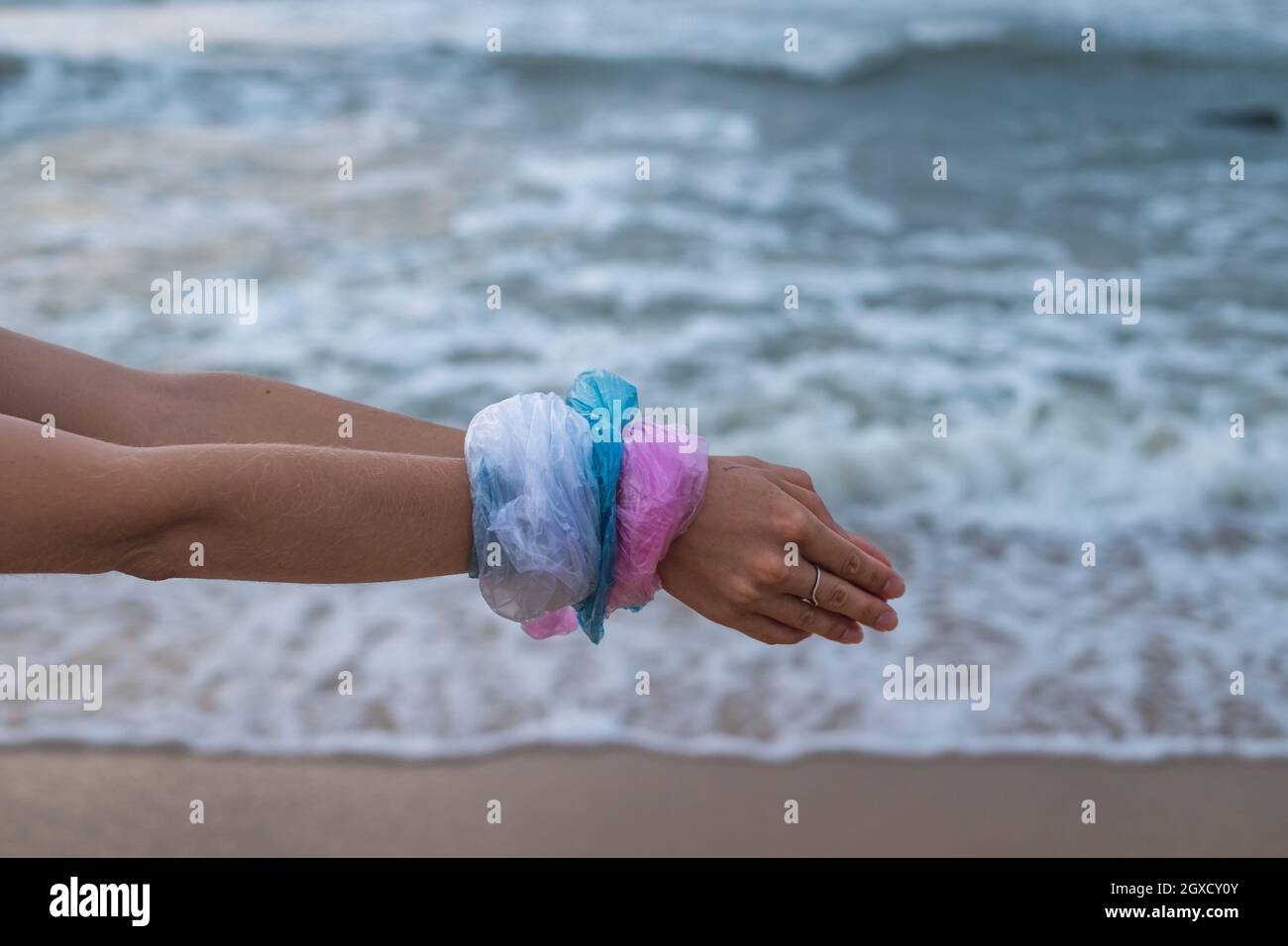 Frauenhände in blaue, rosa und weiße Plastiktüten am Strand eingewickelt. Meer im Hintergrund. Konzept der Kunststoff-Verschmutzung zu stoppen, Kunststoff frei Stockfoto