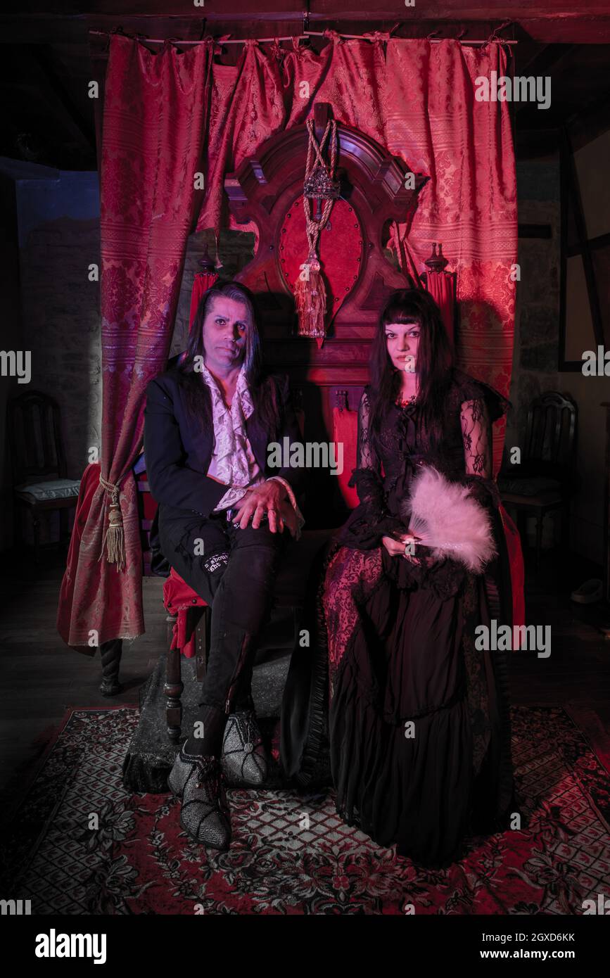 Mann und Frau in gotischen Kleidern sitzen auf einem Thron in einem mittelalterlichen Setting. Vampire. Stockfoto