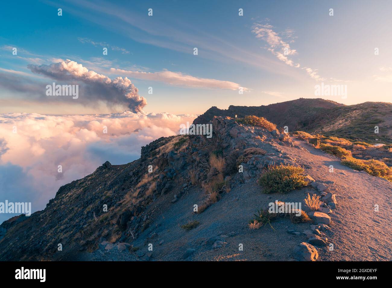 Sonnenaufgang auf einem Höhenweg inmitten weicher, dicker weißer Wolken und dem Ausbruch eines Vulkans im Hintergrund. Cumbre Vieja vulkanische Eruptio Stockfoto