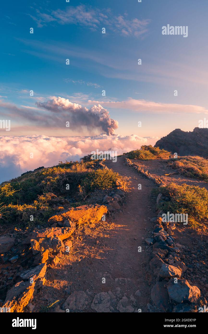 Sonnenaufgang auf einem Höhenweg inmitten weicher, dicker weißer Wolken und dem Ausbruch eines Vulkans im Hintergrund. Cumbre Vieja vulkanische Eruptio Stockfoto