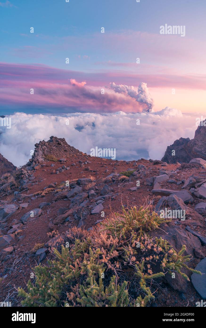 Sonnenaufgang auf mächtigen Berggipfeln inmitten weicher, dicker weißer Wolken und im Hintergrund der Ausbruch eines Vulkans. Cumbre Vieja Vulkanausbruch in La Stockfoto