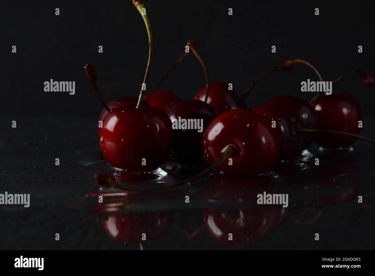 Kirschen, mit Wassertropfen auf schwarzem Hintergrund mit Spiegelung Stockfoto