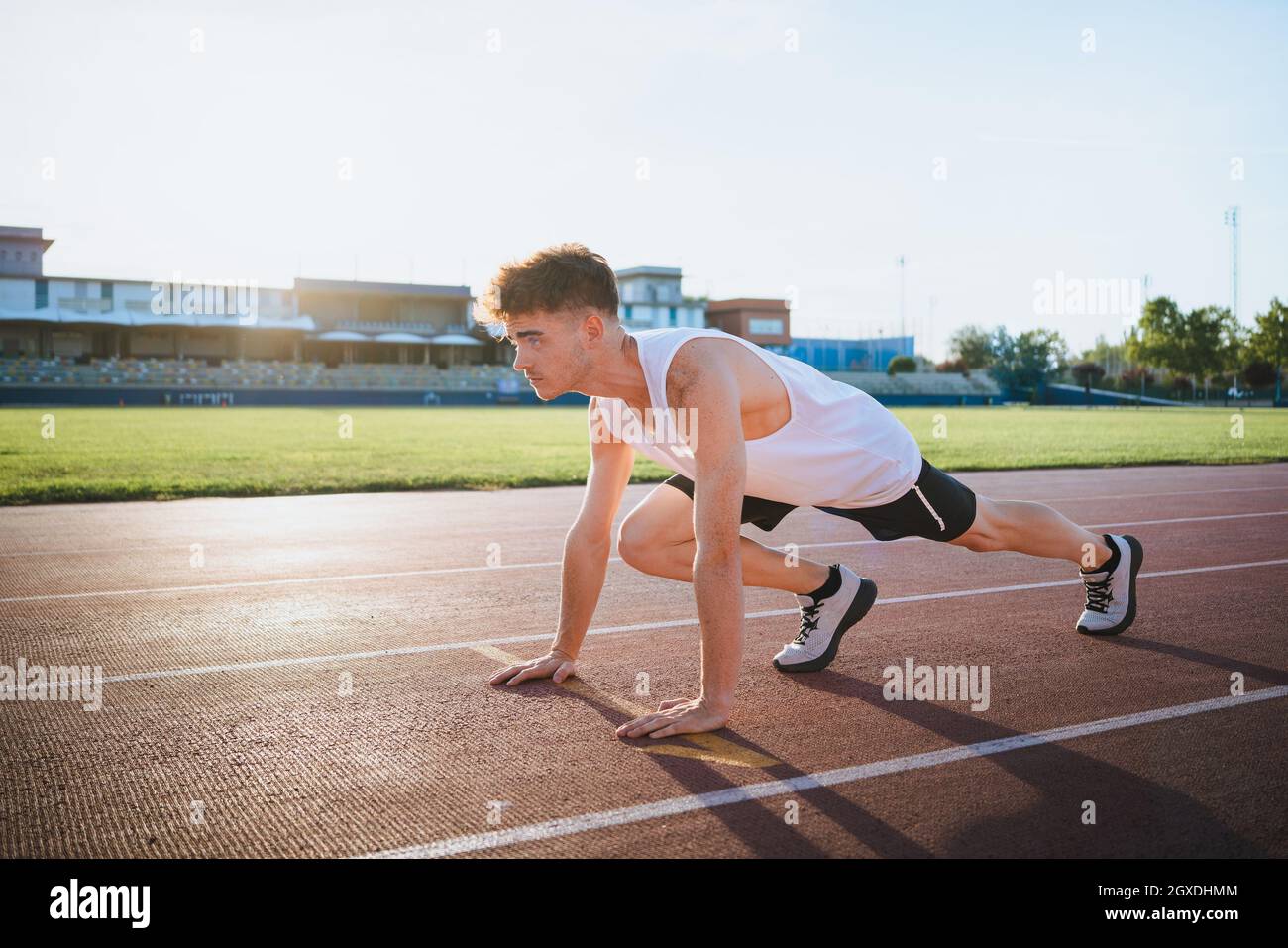 Seitenansicht männlicher Athlet in Sneakers, der in Startposition steht, bevor er im Sonnenlicht auf der Strecke trainiert Stockfoto