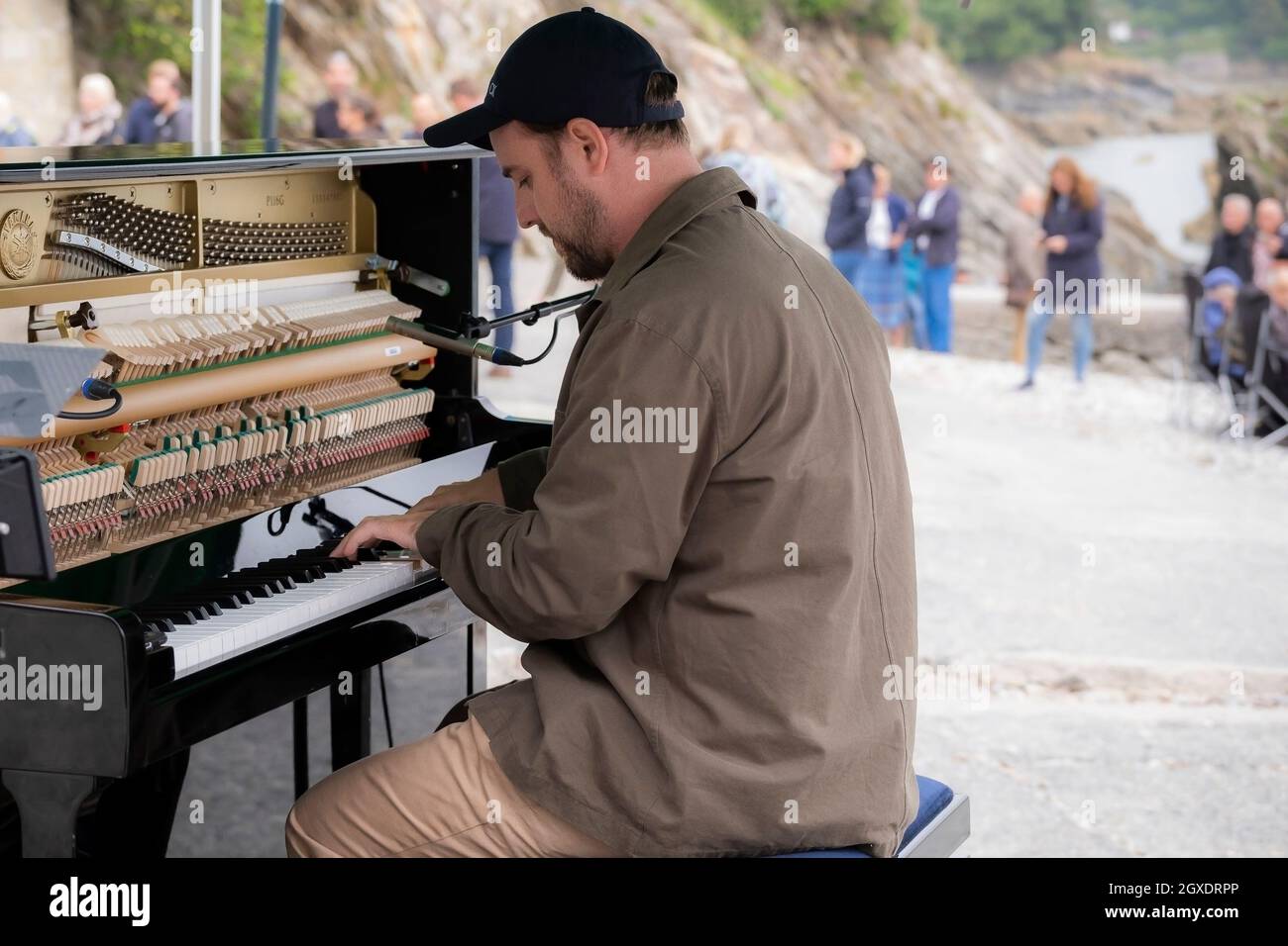 Der zeitgenössische Pianist und Komponist Elliott Jacqués spielt am Trebah Garden Beach in Polgwidden Cove in Cornwall Klavier. Stockfoto