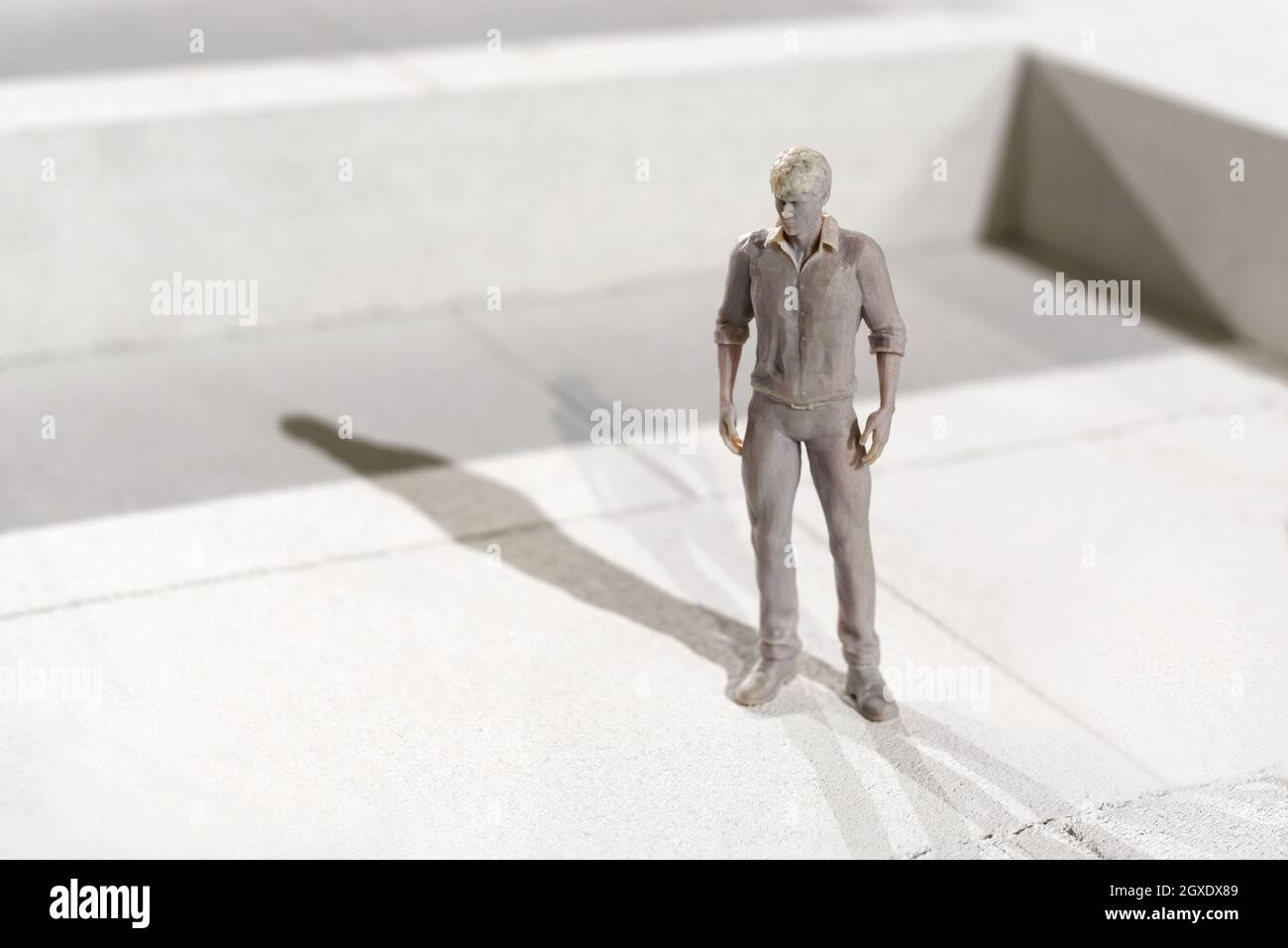 Miniatur 3d gedruckte monochrome Figur eines Mannes in Freizeitkleidung, der auf Fliesen steht und mit Copyspace einen Schatten im Sonnenlicht wirft Stockfoto