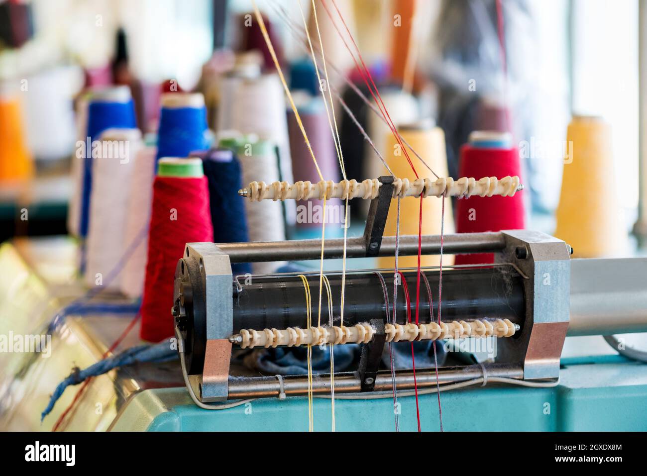 Garnzufuhr mit Wolle mit Gewinde in verschiedenen Farben auf Strickmaschine in einer Strickfabrik in Nahaufnahme Detail Stockfoto