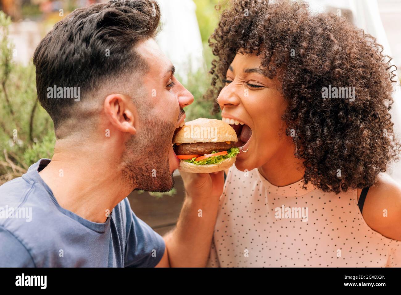Multirassische Männer und Frauen essen zusammen leckere Hamburger während romantischen Date im Restaurant im Sommer Stockfoto