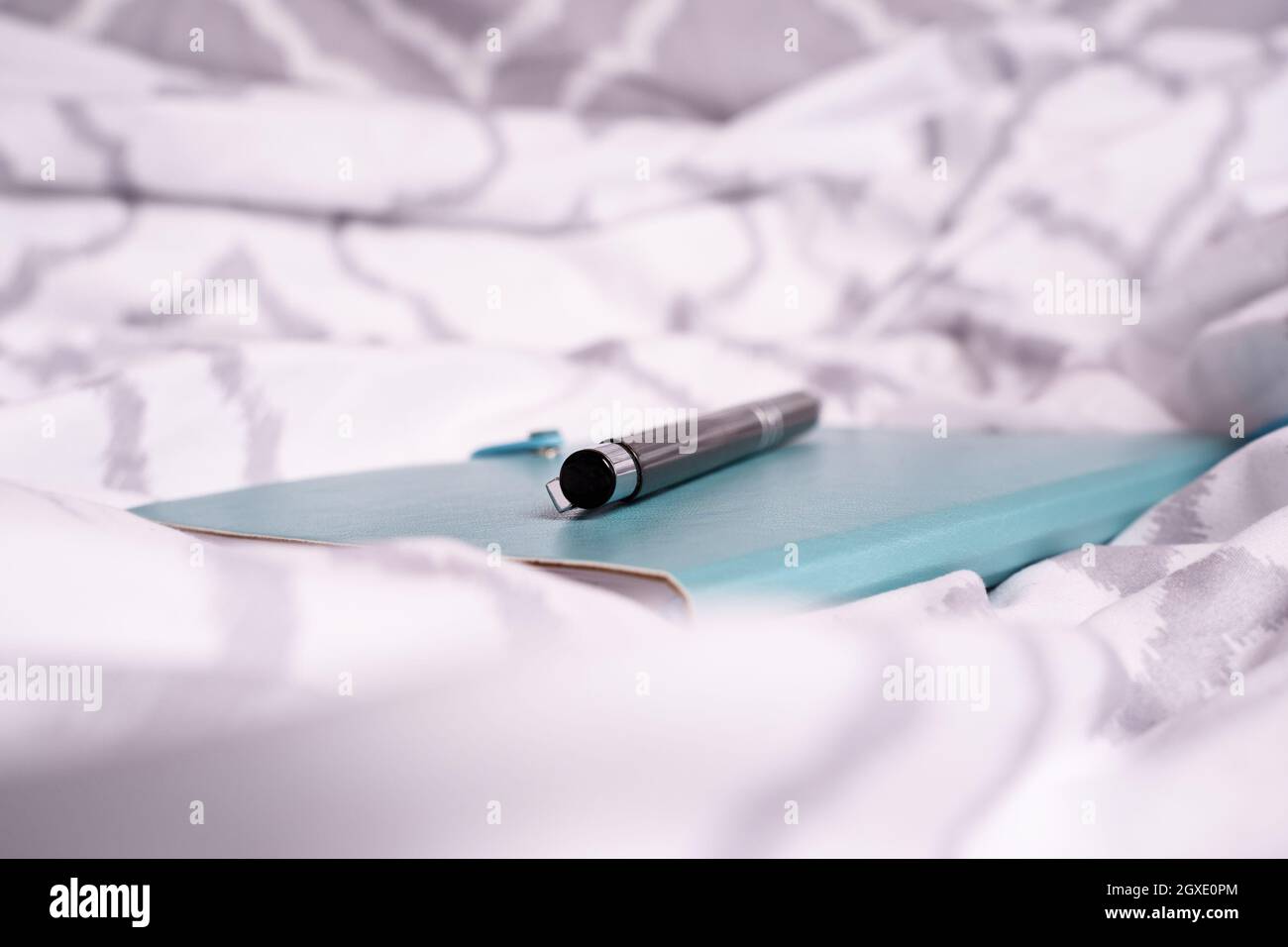 Nahaufnahme von Notizblock und Stift auf dem Bett mit modernen, hellen Bettlaken. Mobiles Arbeitskonzept. Konzept für freiberufliche Bildung, Fernunterricht oder Arbeit von zu Hause aus. Stockfoto