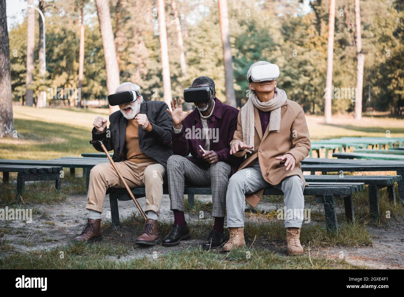 Aufgeregt interracial Männer in vr Headsets sitzen auf Bank im Herbst Park Stockfoto