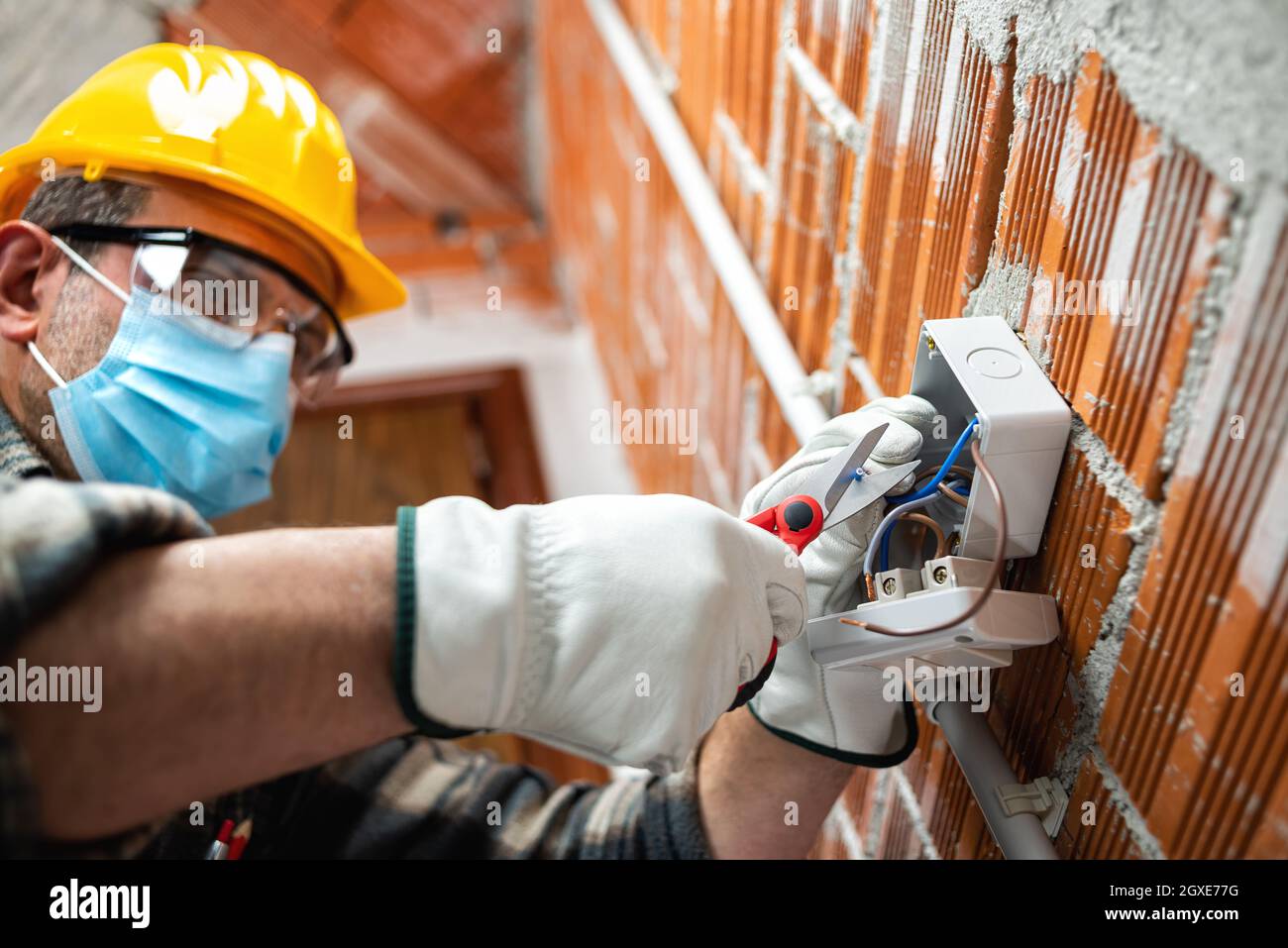 Elektriker Arbeiter mit Schere bereitet die elektrischen Kabel eines elektrischen Systems; tragen Sie die chirurgische Maske, um die Ausbreitung von Coronavirus zu verhindern. Stockfoto