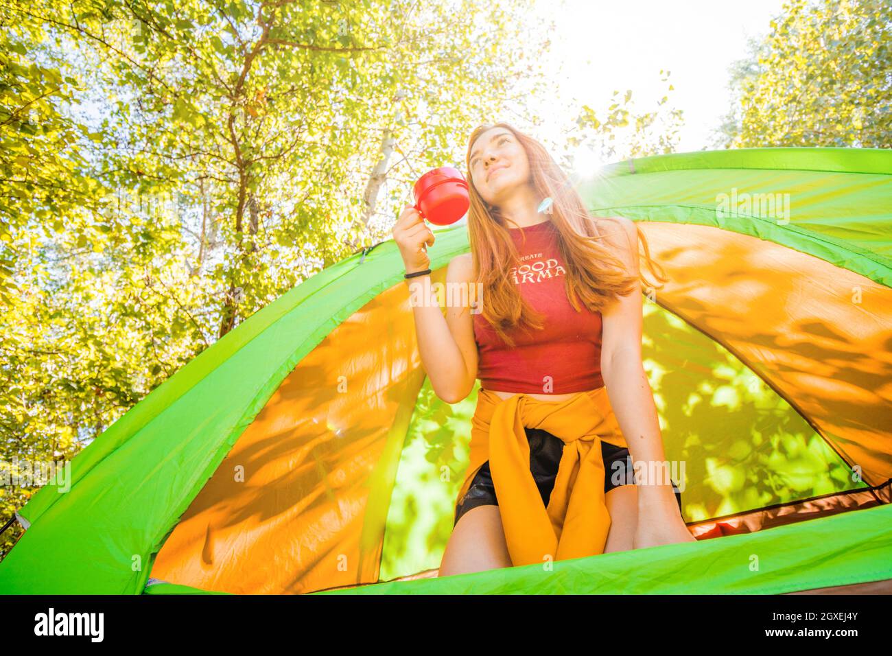 Das junge Mädchen trinkt Kaffee aus einem Touristenbecher, während es in einem Zelt sitzt. Stockfoto