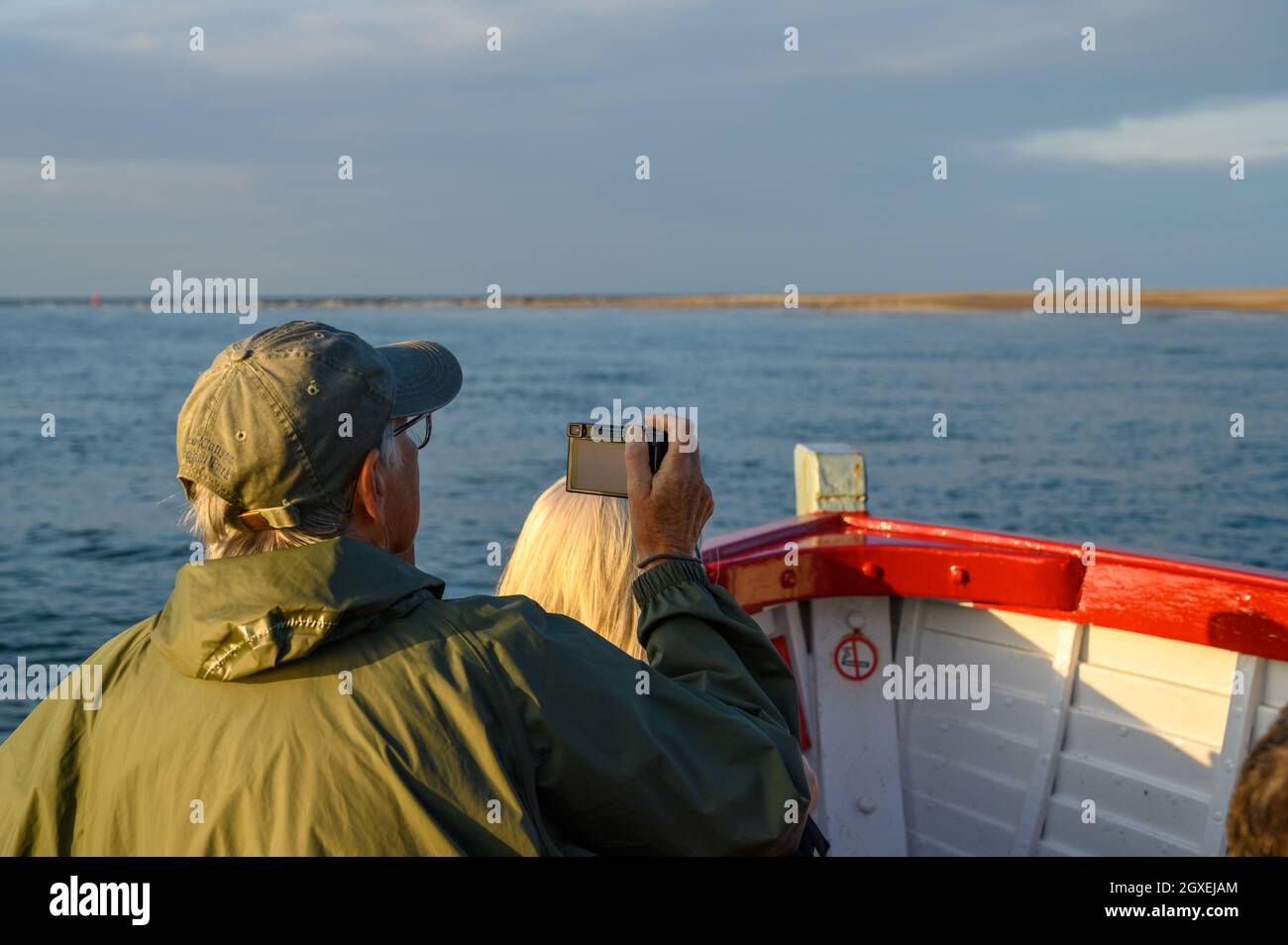 Passagiere an Bord eines Bootes mit Robbencharter beobachten und fotografieren Robben, die sich im niedrigen Sonnenlicht in Blakeney Point, Norfolk, England sonnen. Stockfoto