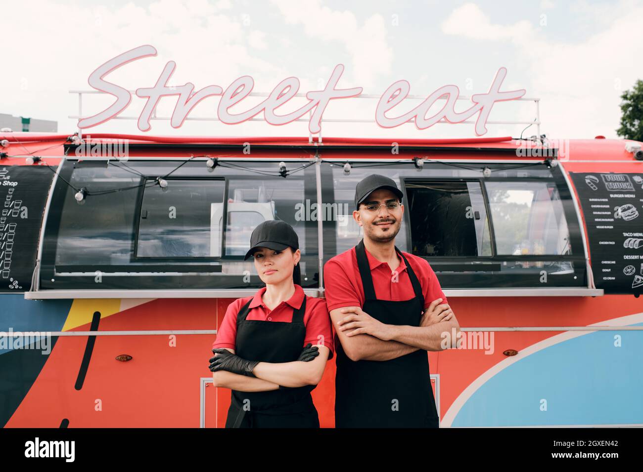 Zwei junge erfolgreiche Kollegen in Uniform stehen gegen den Street Food Truck Stockfoto