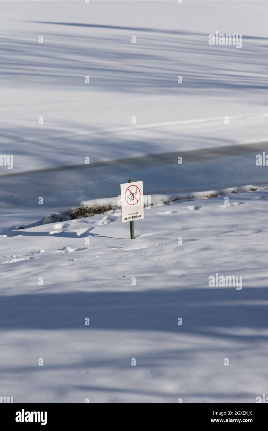 Winterfluss mit Schnee und Eis bedeckt und ein Verbotsschild "Angeln ist verboten" in russischer Sprache vertikale Ausrichtung Stockfoto