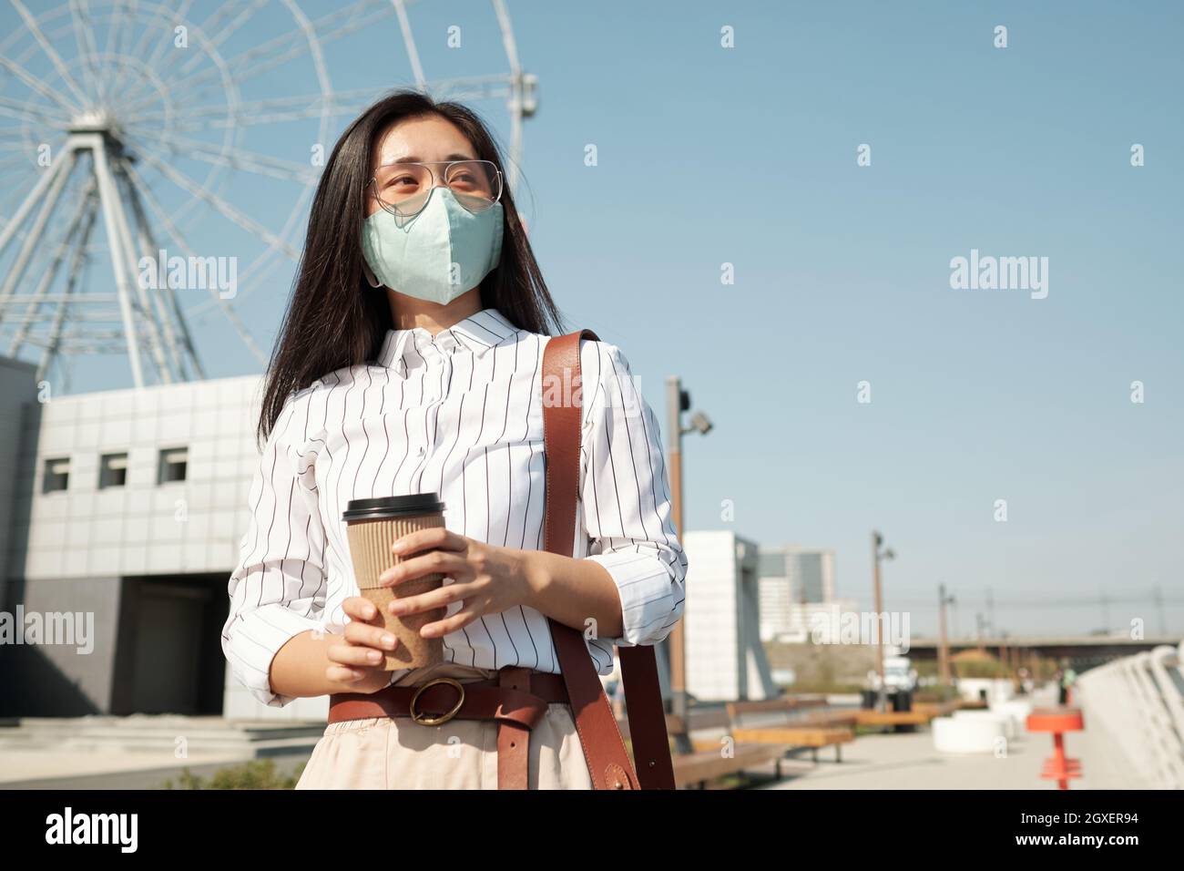 Junge Geschäftsfrau in Schutzmaske mit Kaffeepause im Freien Stockfoto