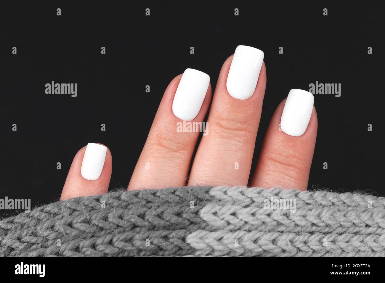 Weibliche Hand mit grauem Strickschal mit schöner Maniküre - weiße Nägel. Nagelpflegekonzept Stockfoto