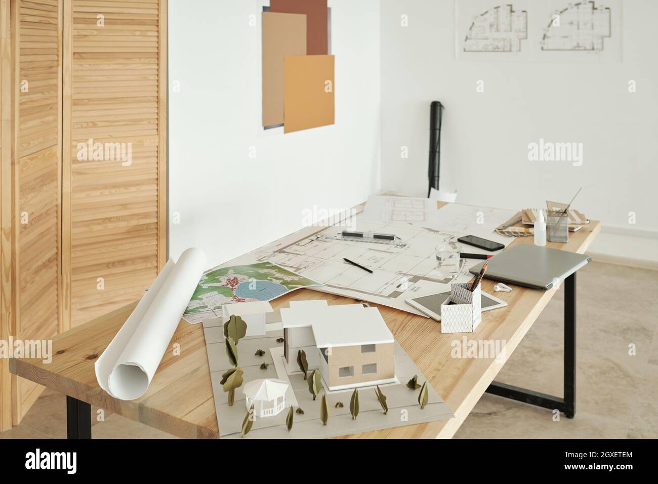 Holztisch mit Papierhausmodellen, Skizzen von Neubauten und mobilen Gadgets Stockfoto