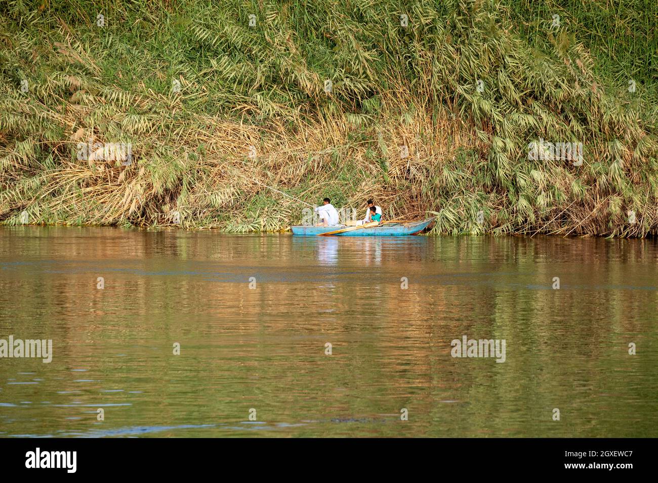 Zwei Nilfischer mit einem kleinen Jungen, der ein kleines Boot rudert und in der Nähe des Ufers in ruhigem Wasser anfischt Stockfoto
