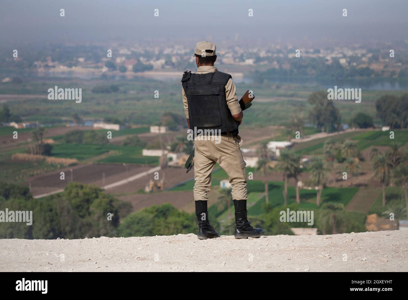 Die Rückansicht eines ägyptischen Sicherheitssoldaten, der ein Gewehr in der Hand hält und von den Felsgräbern von Beni Hassan aus über das Niltal blickt. Stockfoto