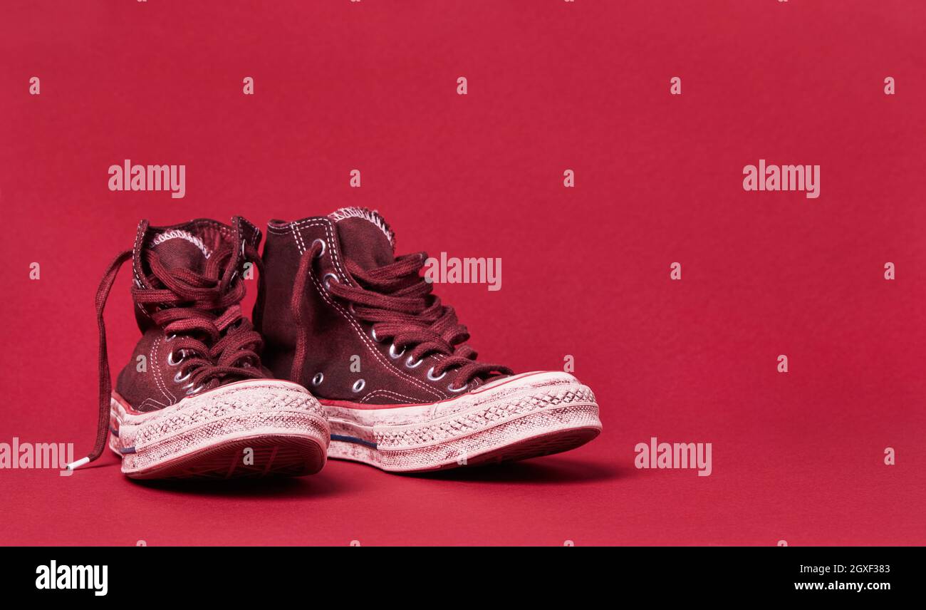 Gebrauchte Segeltuchschuhe auf burgunderrotem Hintergrund Stockfoto