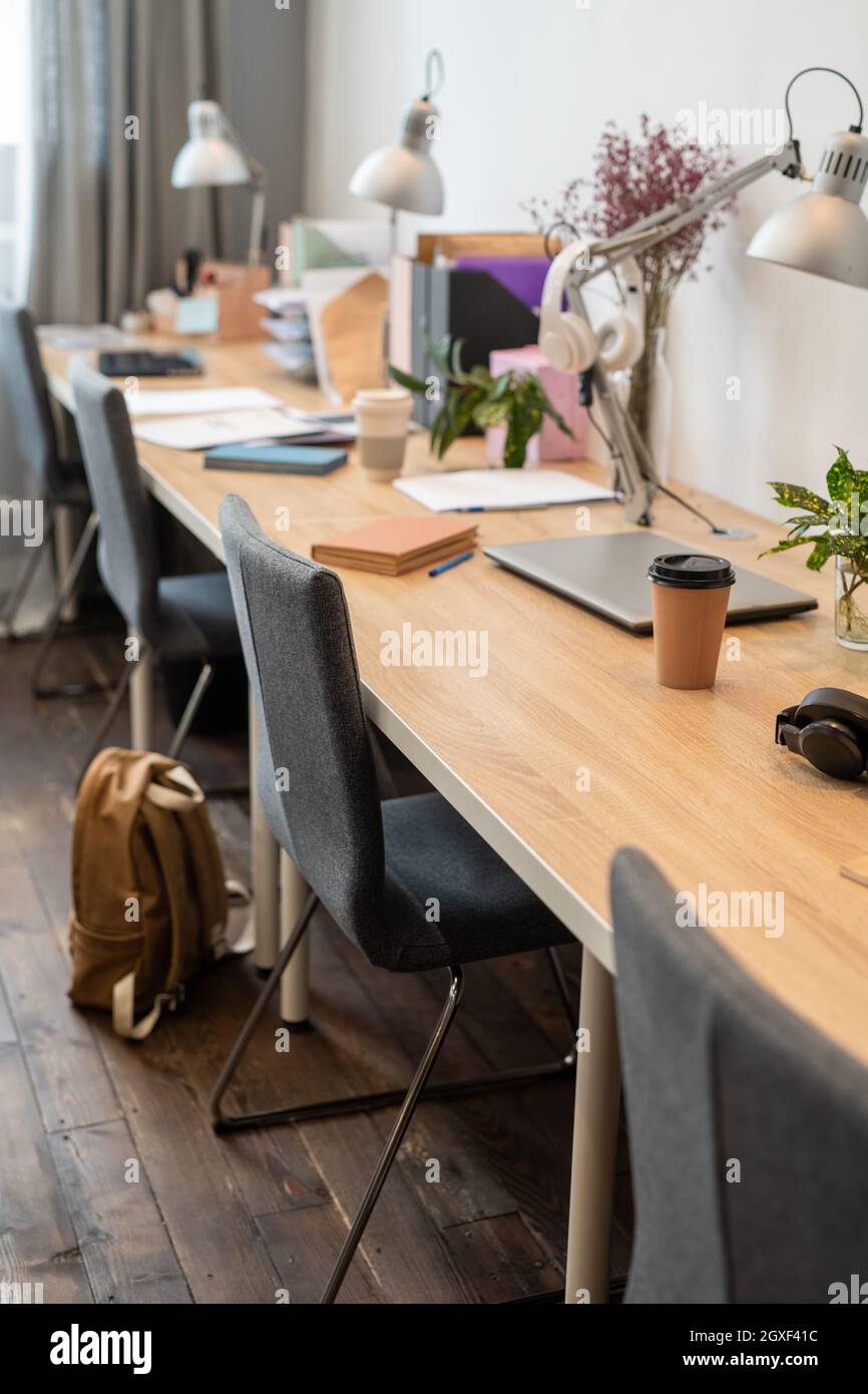 Langer Holzschreibtisch mit Lampen und Stühlen, die in einem modernen Büro an der Wand stehen Stockfoto