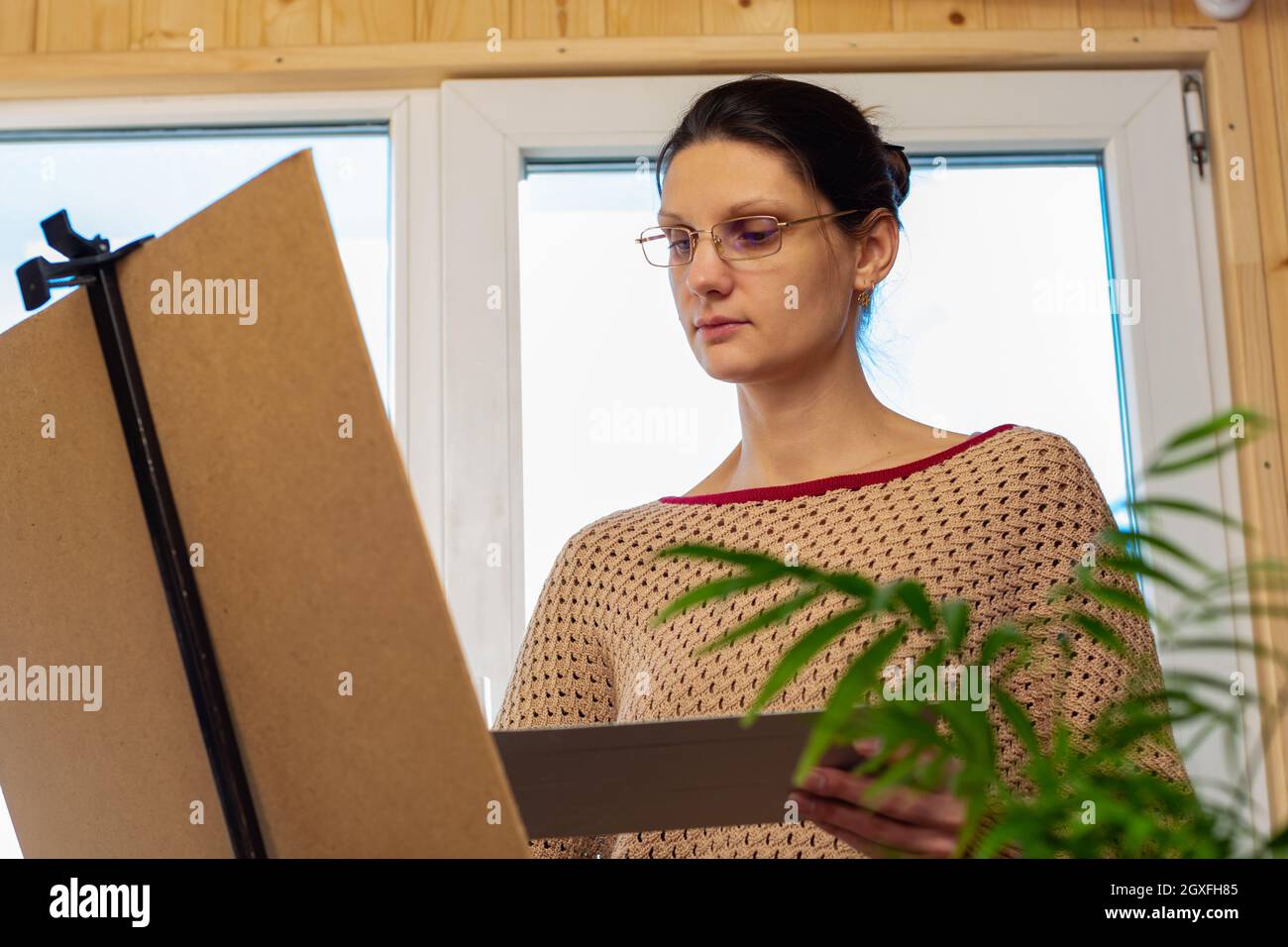 Porträt eines Künstlers bei der Arbeit, ein Mädchen zeichnet eine Zeichnung auf einer Staffelei am Fenster Stockfoto