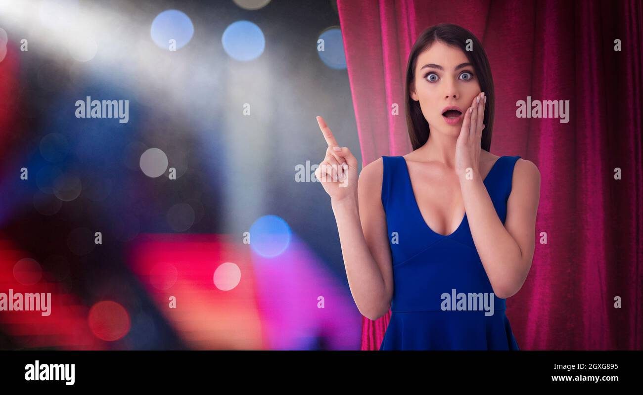 Überrascht hübsche Frau vor roten Vorhängen zeigt etwas über die Theatershow Stockfoto