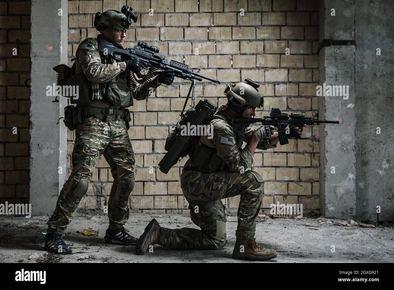 Ein Paar US Army Rangers mit Maschinengewehr und Gewehr, die sich auf Militärmission entlang der Mauer nach und nach bewegen Stockfoto