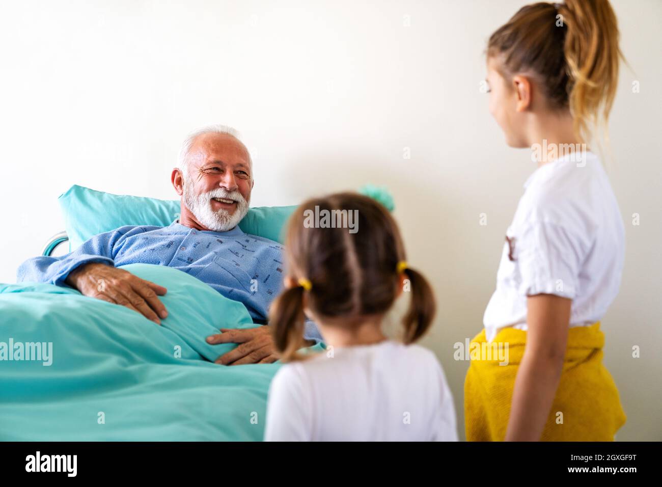 Glückliche Enkelkinder, die Großvater auf der Krankenhausstation besuchen. Support-, Familien- und Gesundheitskonzept. Stockfoto