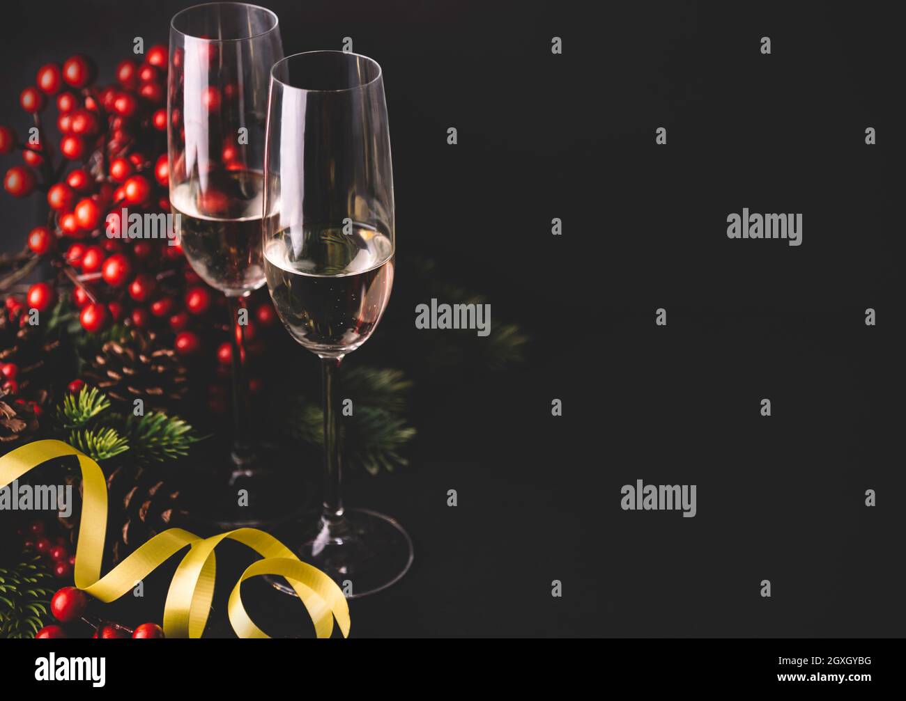 Sektflöten und weihnachtsdekoration mit Nadelbaum, roten Beeren und Pinecone auf schwarzem Hintergrund. Luxus Urlaub Restaurant Abendessen. Neues Jahr Stockfoto