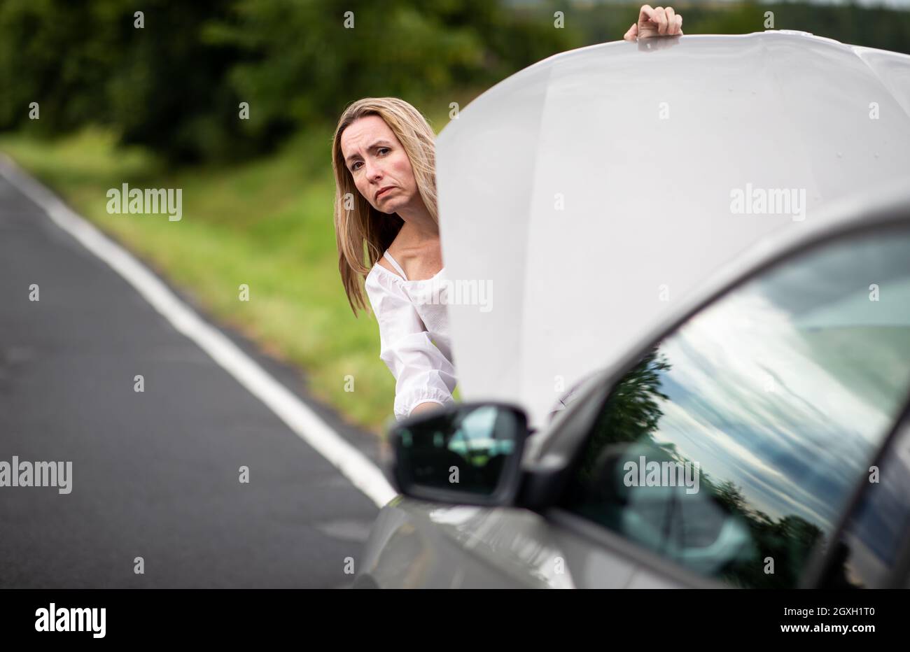 Ziemlich Frau mittleren Alters, die Autoprobleme hat - zusammengebrochenes Auto auf der Seite der Straße, die Versicherungsgesellschaft um Hilfe zu rufen Stockfoto