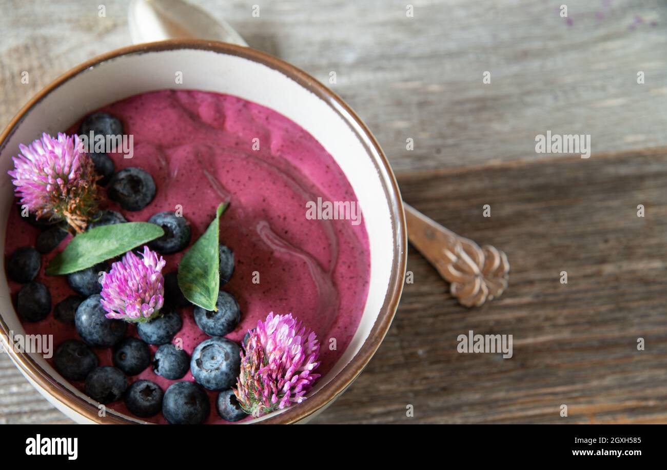 Hausgemachter Heidelbeerjoghurt mit roten Kleeblumen auf Holztisch. Stockfoto