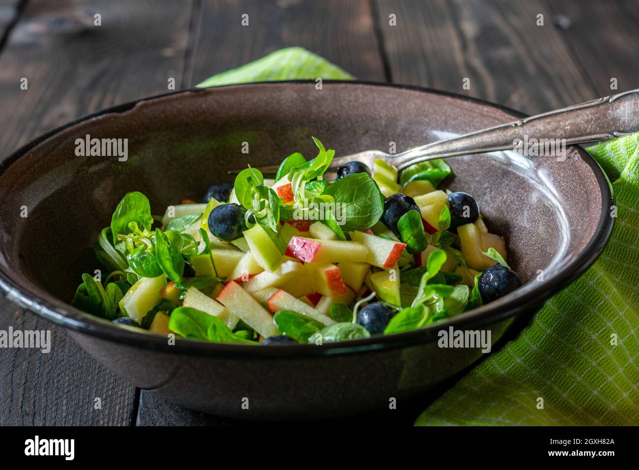 Bio-Obstsalat mit Lammlattuce´s. Mit Olivenöl und Apfelessig mariniert. Serviert in einer rustikalen braunen emaillierten Schüssel auf einem Holztisch. Stockfoto
