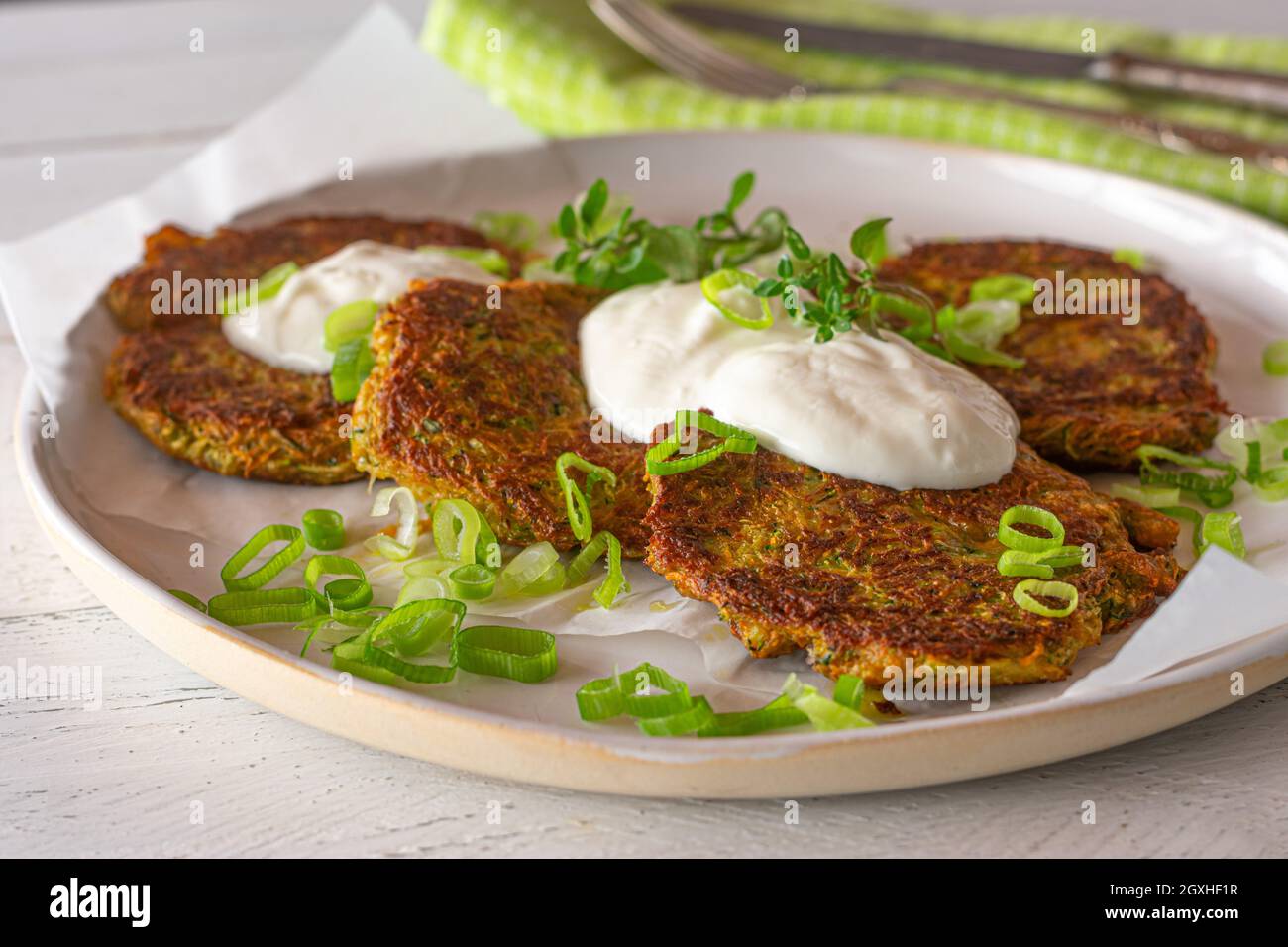 Gesundes glutenfreies Gericht mit Gemüsepfannkuchen, gebacken mit Karotten und Zucchini, serviert mit griechischem Joghurt-Dip und Kräutern auf einem weißen Teller. Stockfoto