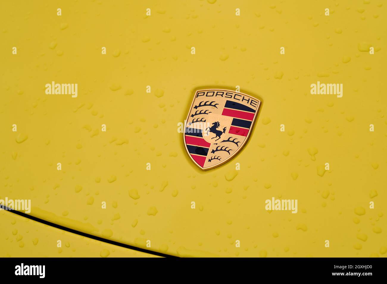 Nahaufnahme des Porsche-Logos auf einem gelben Auto mit Regentropfen. Ferdinand Porsche gründete das Unternehmen 1931 mit Hauptsitz im Zentrum von Stuttgart. Stockfoto