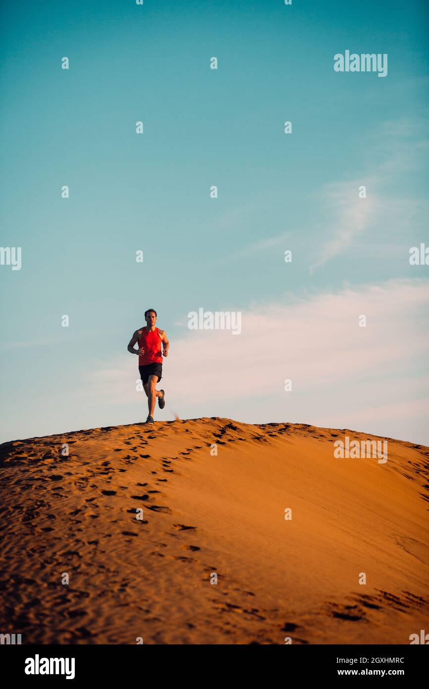 Running man Athlet Silhouette läuft über Wüste Düne weit weg in Sonnenuntergang. Sommertag Aufwärmen Sporttraining . Vertikaler Hintergrund Stockfoto
