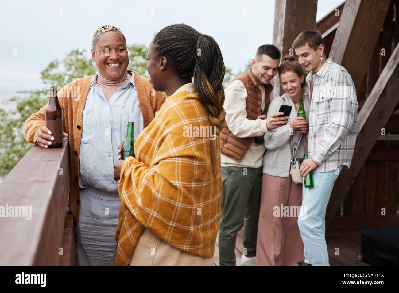 Verschiedene Gruppen junger Menschen trinken Bier auf dem Balkon während der Party am Lake House Stockfoto