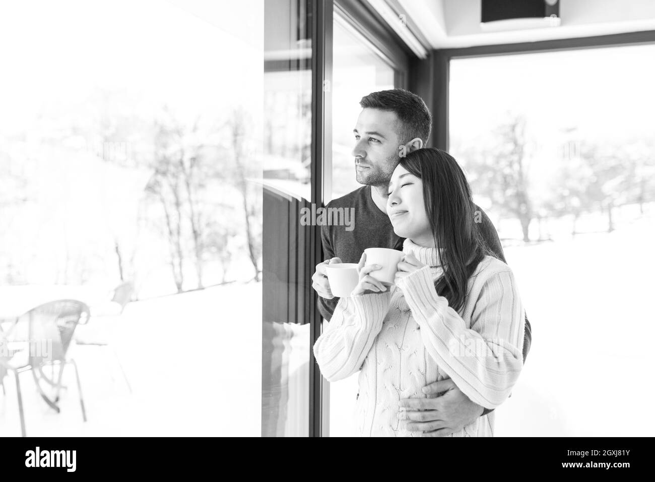 Glückliche junge Multiethnischen Paar beim Kaffee am Morgen durch das Fenster in der Kälte des Winters Tag zu Hause Stockfoto