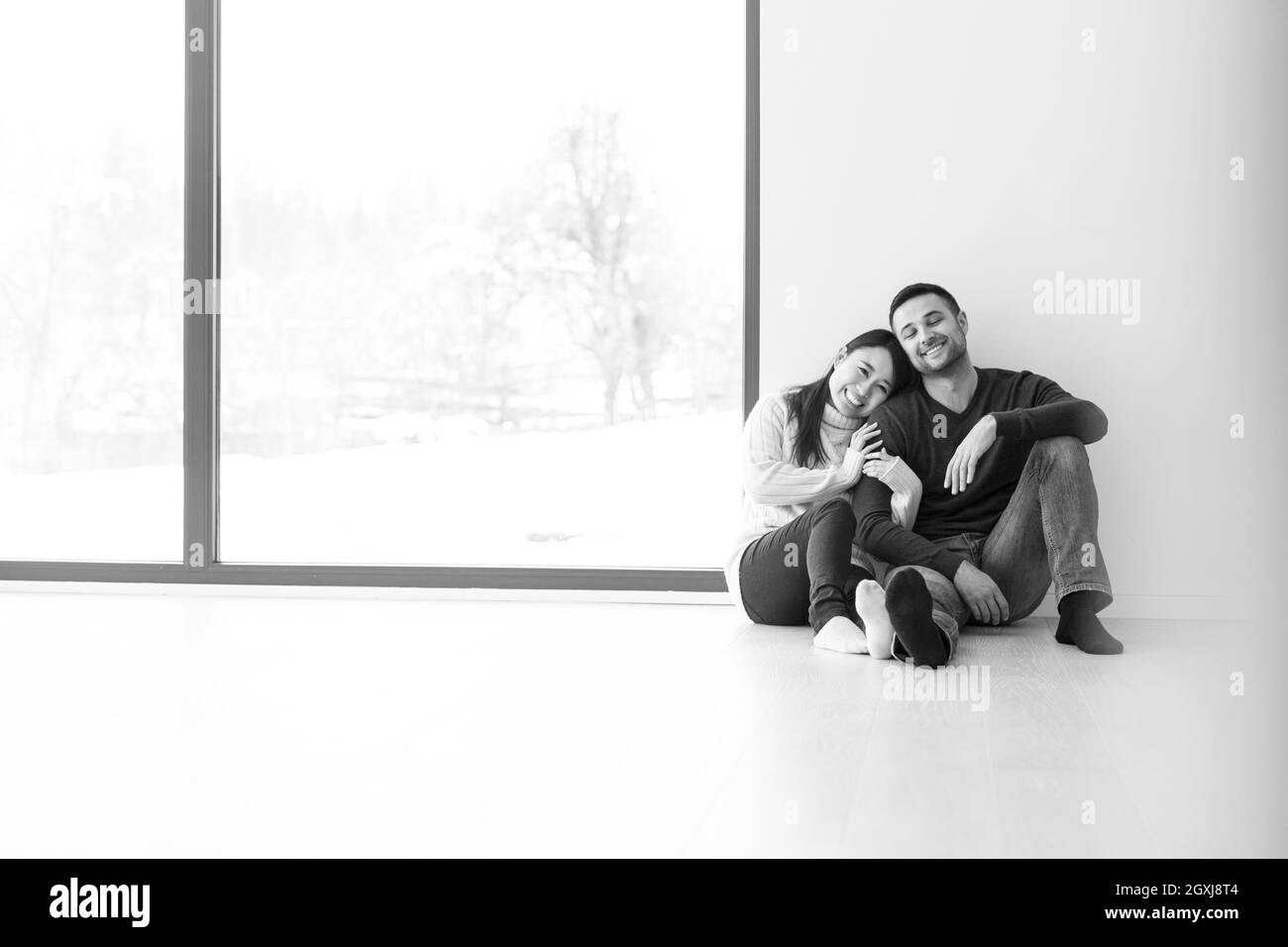 Glückliche junge Multiethnischen Paar in der Nähe der Fenster zu Hause auf kalten Wintertag sitzt Stockfoto
