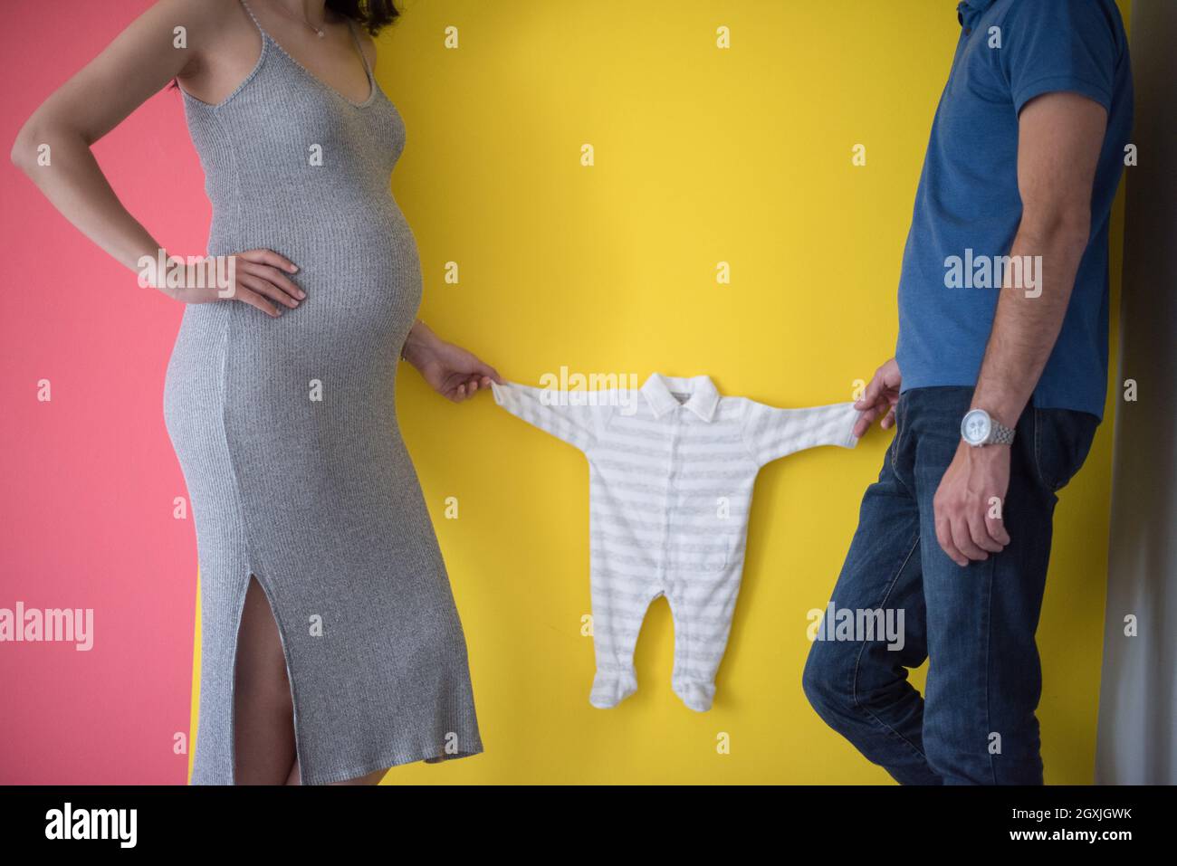 Schöne schwangere Frau und ihr Ehemann erwartet baby Holding Baby Bodys und lächelnd über bunten Hintergrund Stockfoto