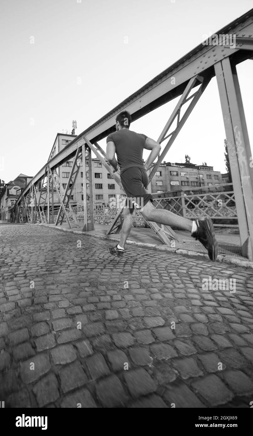Junge sportliche Mann joggen auf der anderen Seite der Brücke am sonnigen Morgen in der Stadt Stockfoto