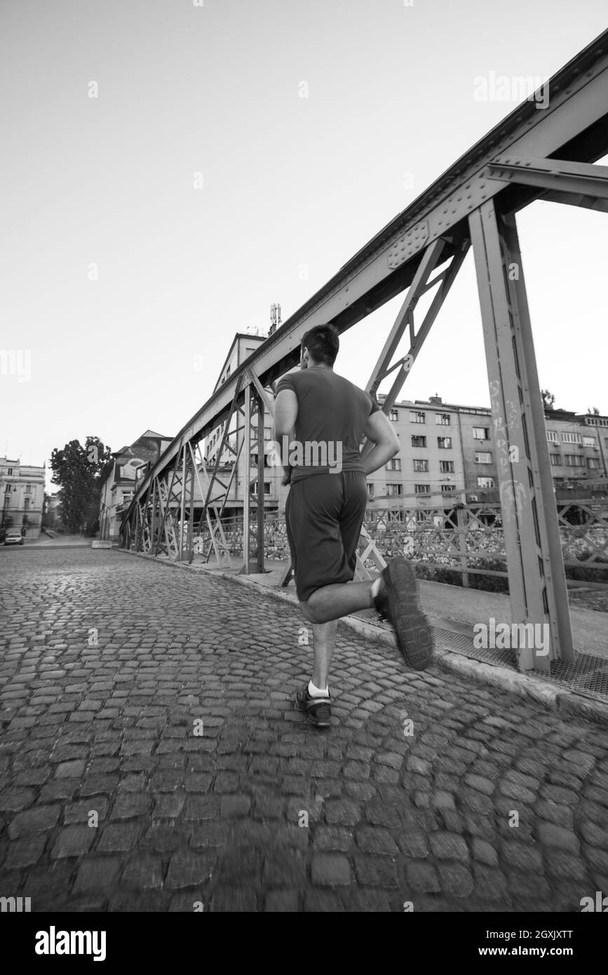 Junge sportliche Mann joggen auf der anderen Seite der Brücke am sonnigen Morgen in der Stadt Stockfoto