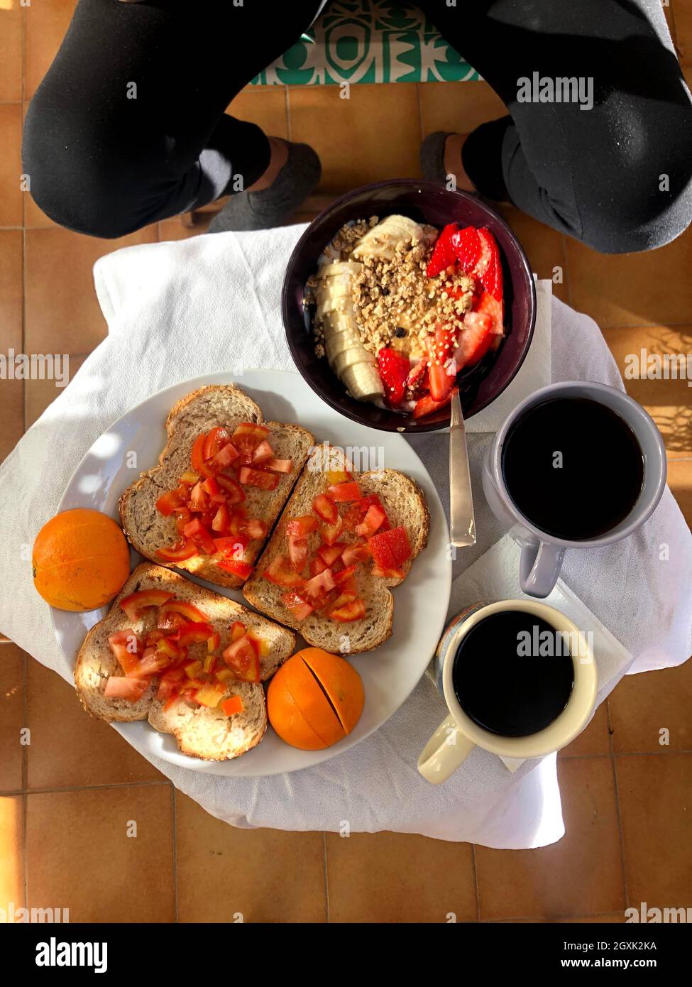 Frau genießt das Frühstück mit Kaffee, Toast mit Tomaten und einer Porridge Schüssel mit Bananen und Erdbeeren Stockfoto