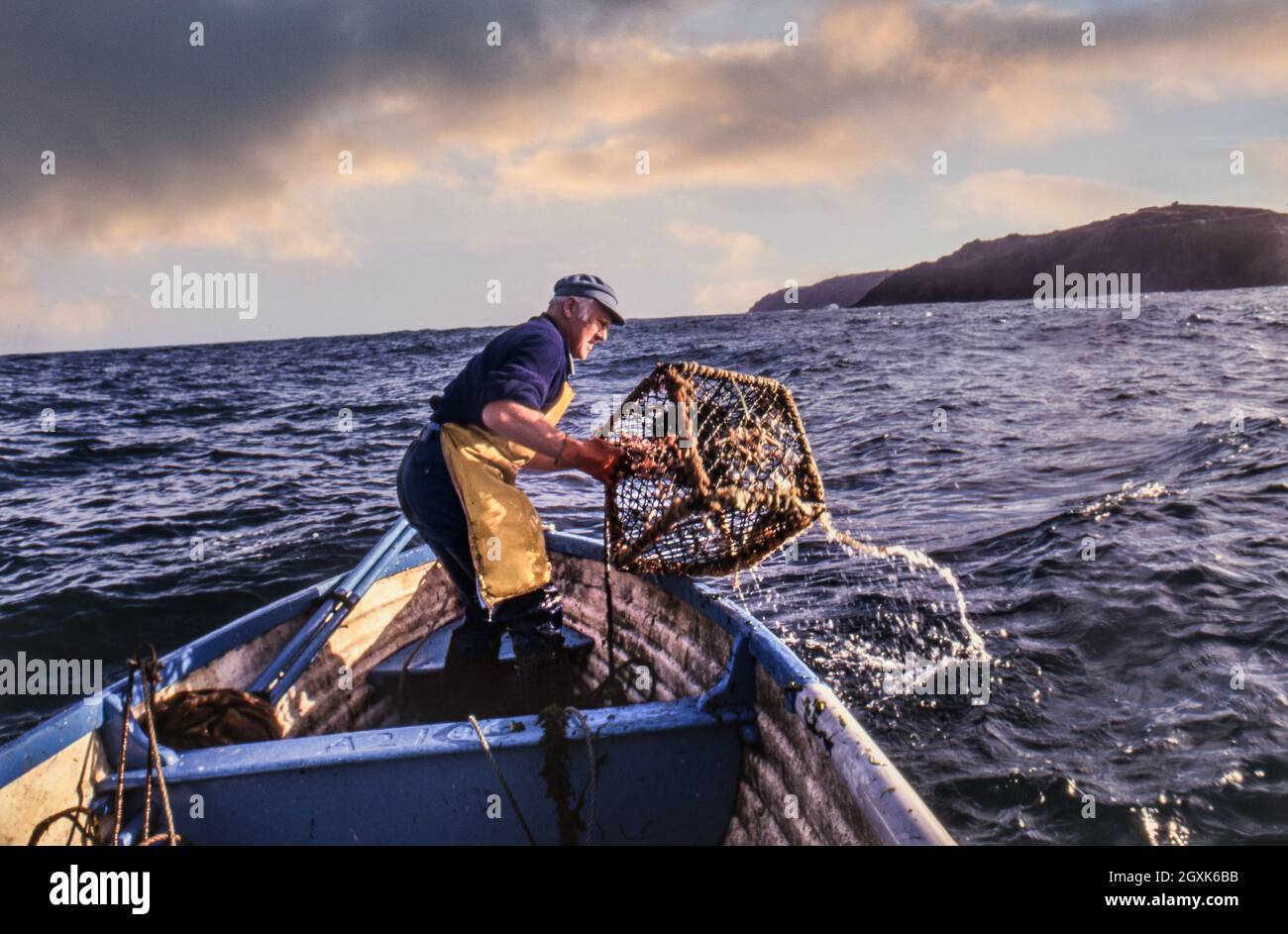 Hummer/Krabben Britischer Fischer auf See in einem kleinen offenen Boot, das seine Hummertöpfe bei Sonnenaufgang vor der Cornwall-Küste in Großbritannien herausnimmt Stockfoto