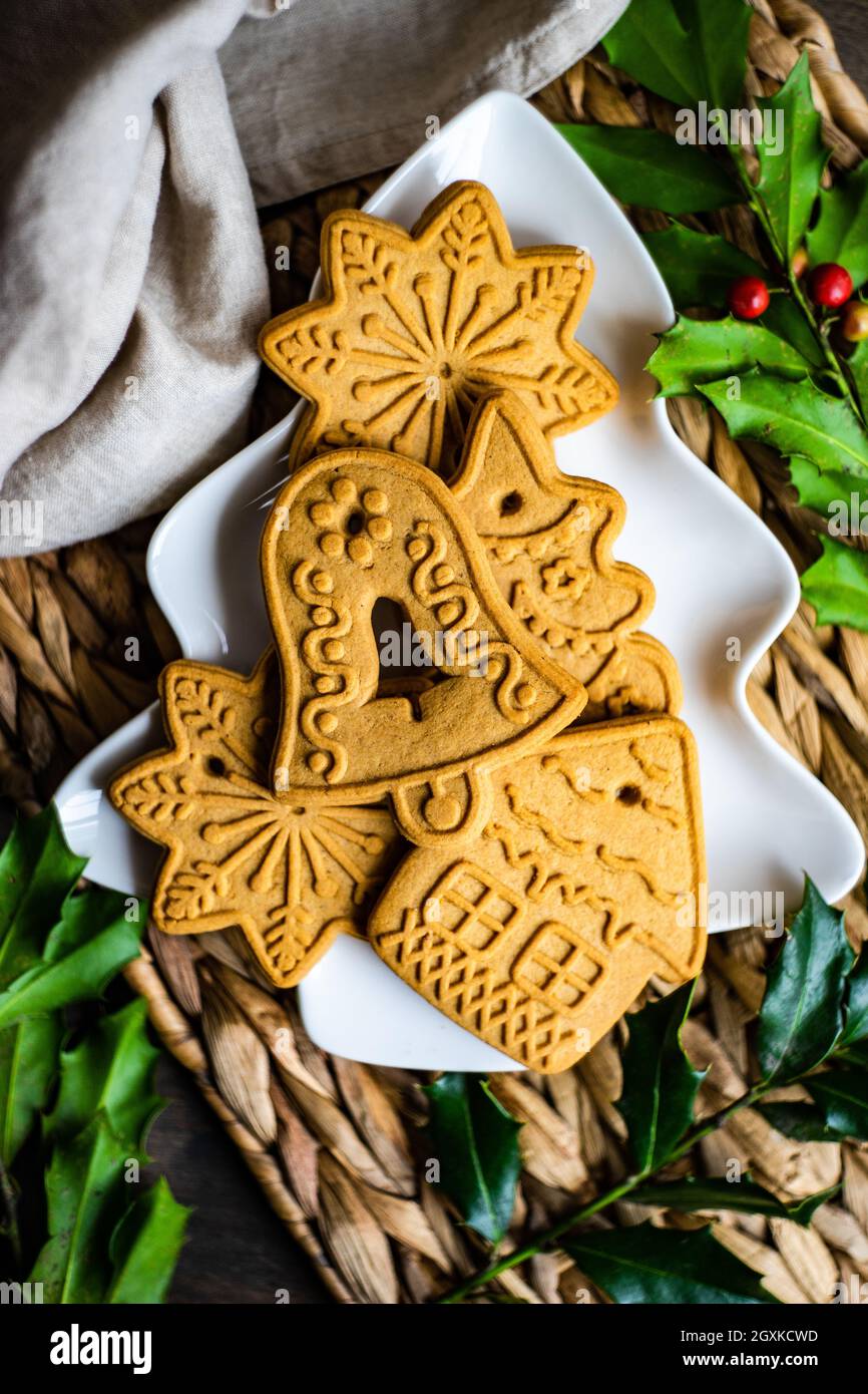 Weihnachts-Lebkuchenkekse auf einem baumförmigen Teller mit frischem Stechpalme Stockfoto